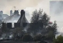 A British flag flies amongst the smoldering ruins of houses as fire services tackle a large blaze on July 19 in Wennington, England. A series of grass fires broke out amid an intense heatwave.