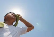 A man wiping sweat from his face under the hot sun.