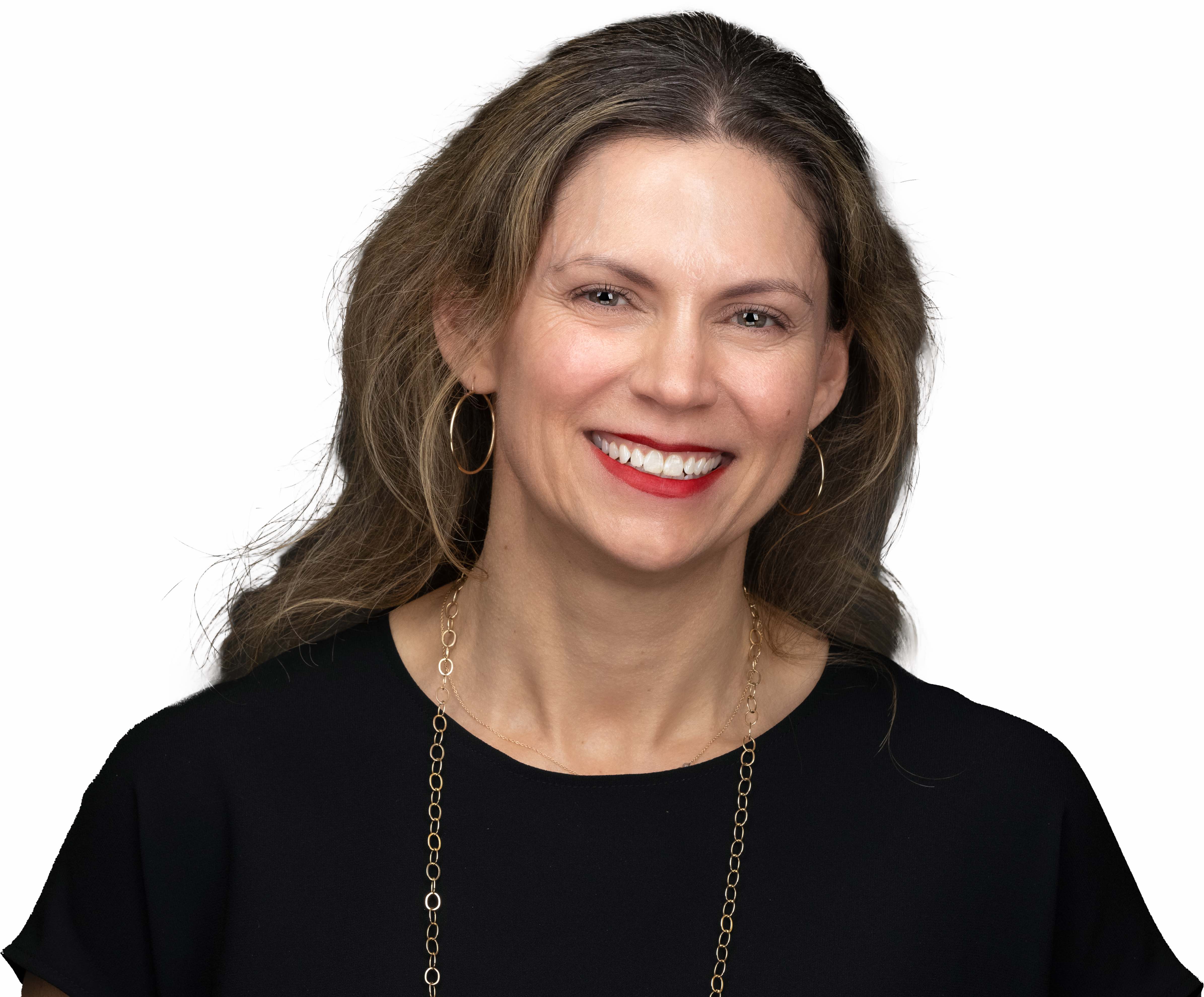 Consejos de directoras ejecutivas en tecnología 4 Susan Stone mira a la cámara sonriendo, con la cabeza ligeramente hacia la izquierda. Lleva una camisa negra de cuello barco con un collar de cadena de oro, aretes de aro de oro y lápiz labial rojo.