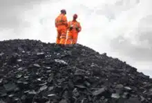 Two coal miners standing on top of a massive pile of coal.