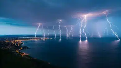 Multiple bolts of lightning strike ground and water along a coastline in Italy. The sky is dark blue.
